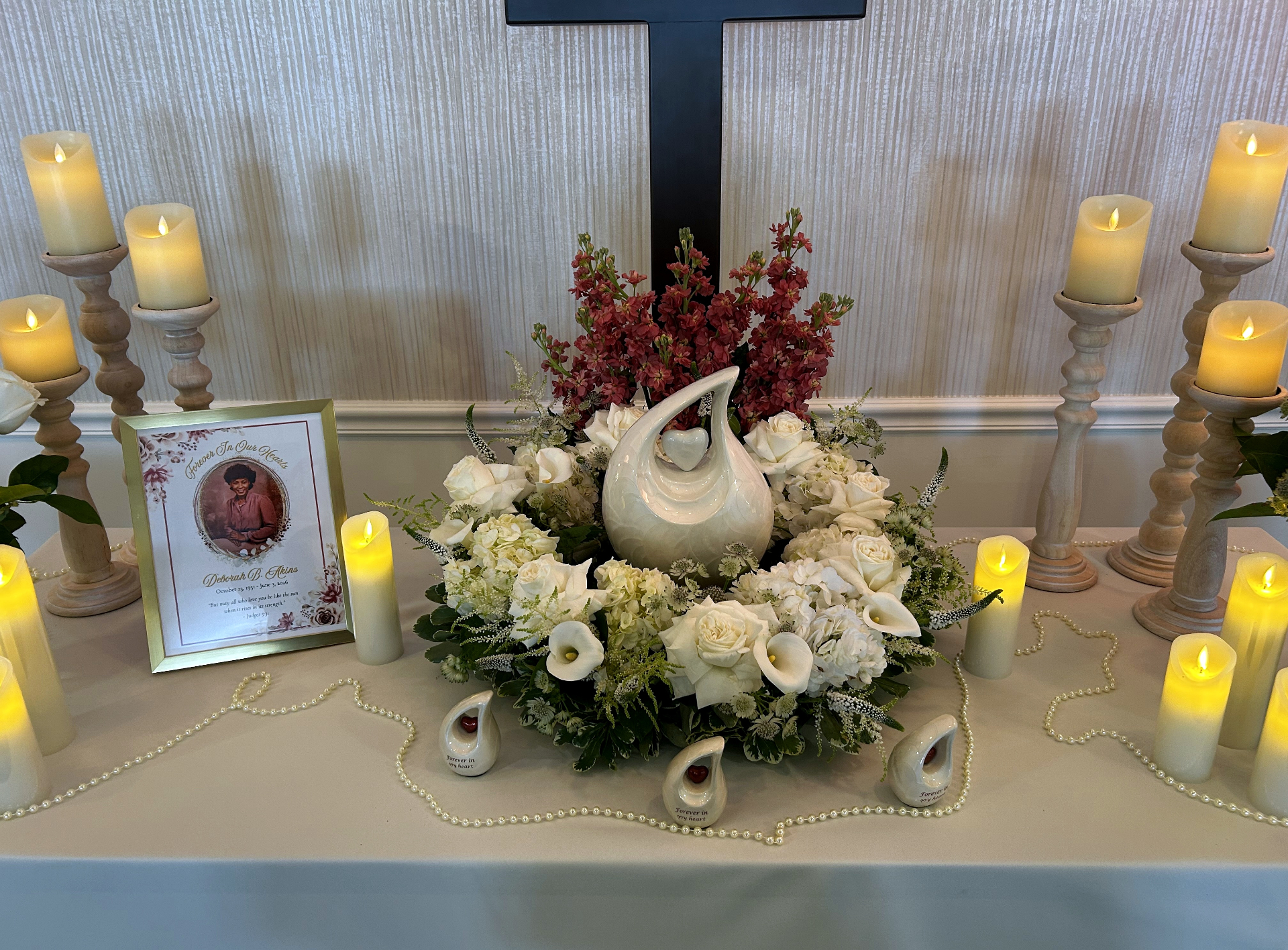Memorial table with urn, white floral wreath, framed portrait of Deborah B. Akins, and flickering candles