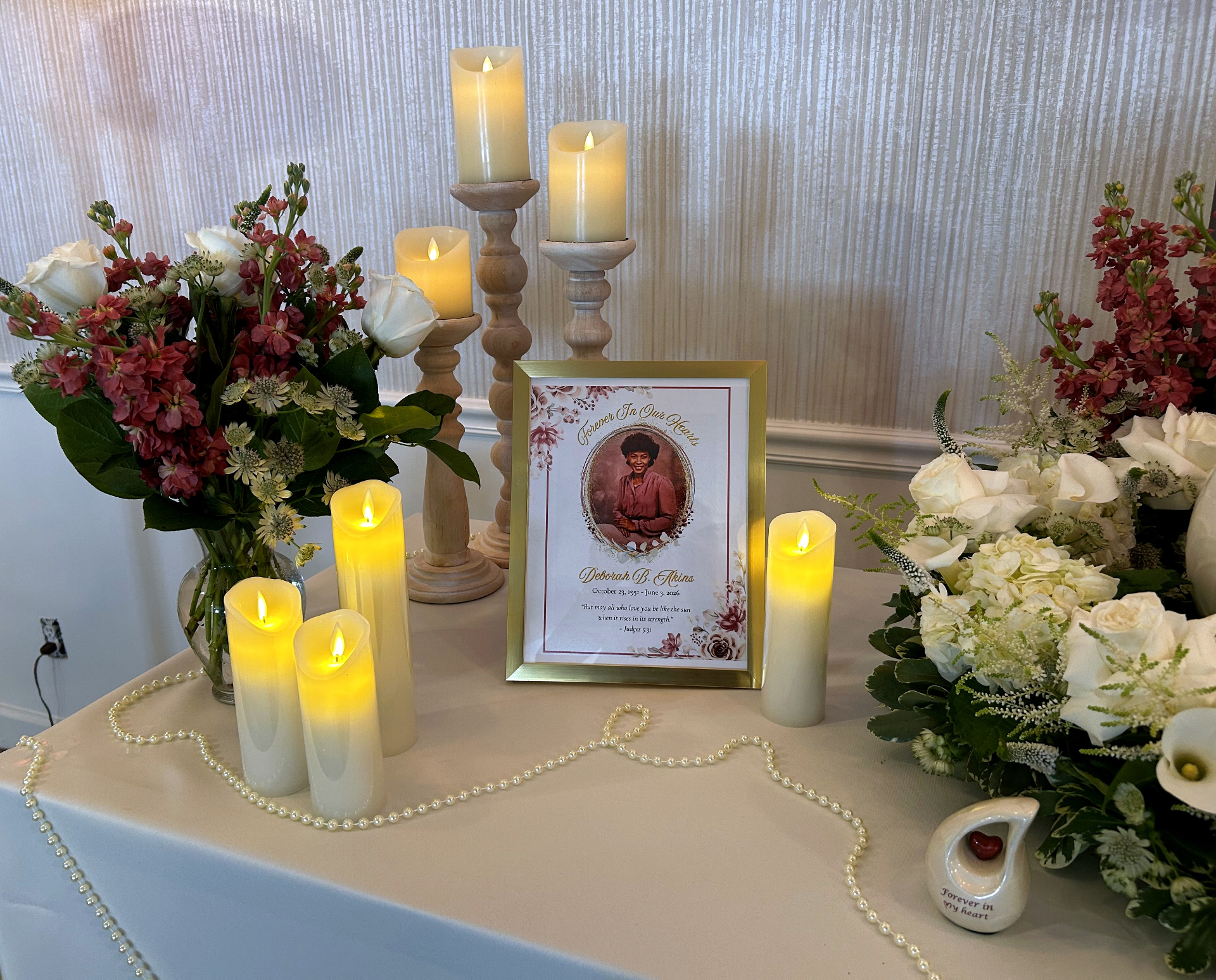 Memorial table setup with framed portrait of Deborah B. Akins, candles, pearls, and floral arrangements
